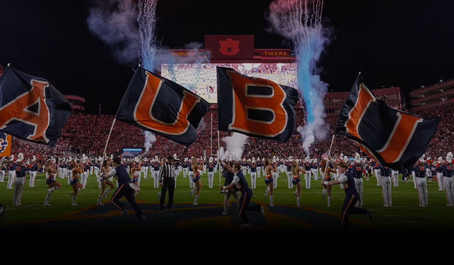 Auburn cheerleaders running flags across the field amid fireworks